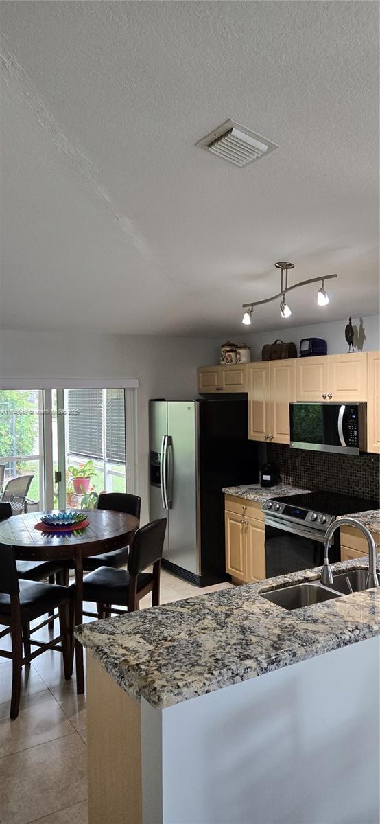 kitchen featuring light stone counters, a sink, visible vents, appliances with stainless steel finishes, and tasteful backsplash