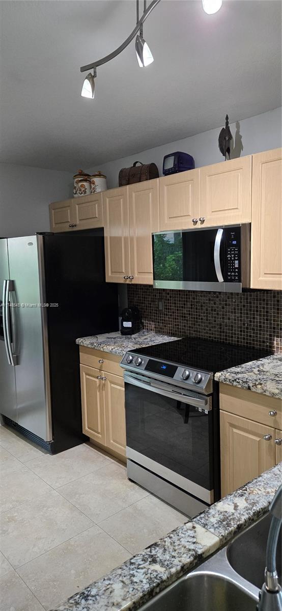 kitchen featuring light tile patterned flooring, stainless steel appliances, light stone counters, and tasteful backsplash