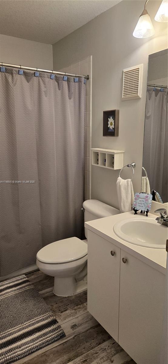 bathroom with toilet, wood-type flooring, a textured ceiling, vanity, and walk in shower