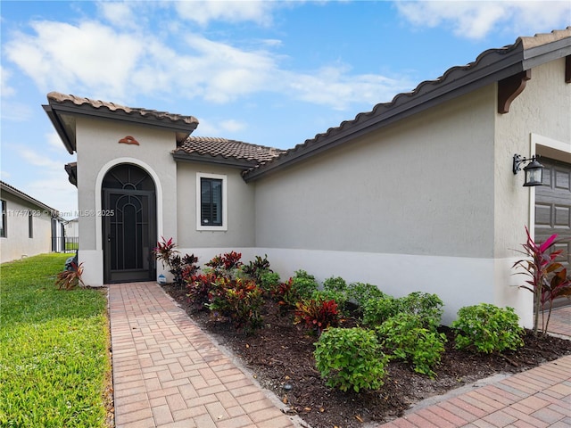 property entrance featuring a tiled roof, stucco siding, a lawn, and a garage