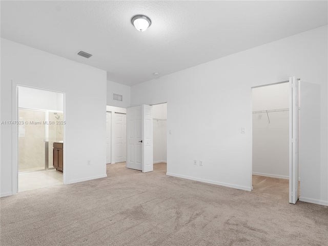 unfurnished bedroom with visible vents, a walk in closet, baseboards, light colored carpet, and ensuite bathroom