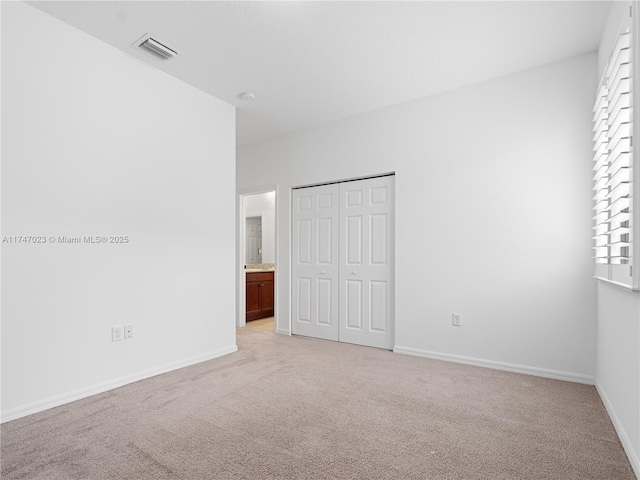 unfurnished bedroom with baseboards, visible vents, a closet, and light carpet