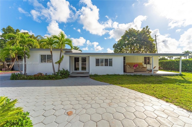 view of front of property featuring french doors, a patio area, a front lawn, and stucco siding