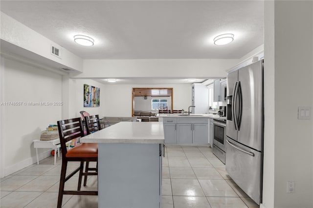 kitchen featuring visible vents, a breakfast bar, stainless steel appliances, a peninsula, and light countertops