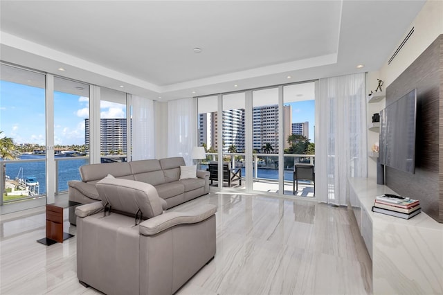 living room featuring floor to ceiling windows, a water view, and a raised ceiling