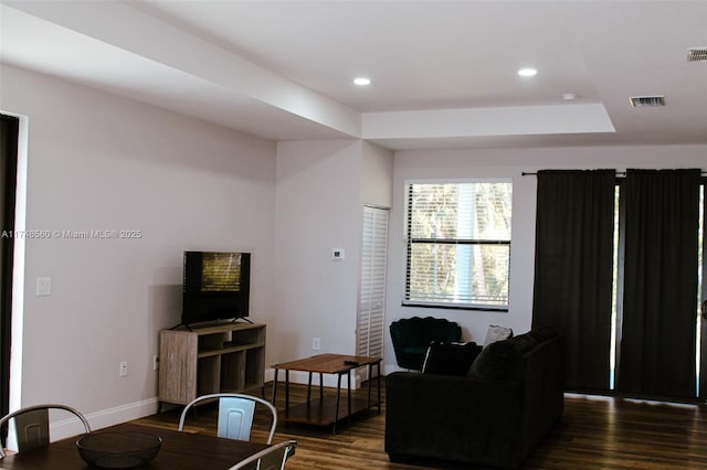 living room featuring a tray ceiling and dark wood-type flooring