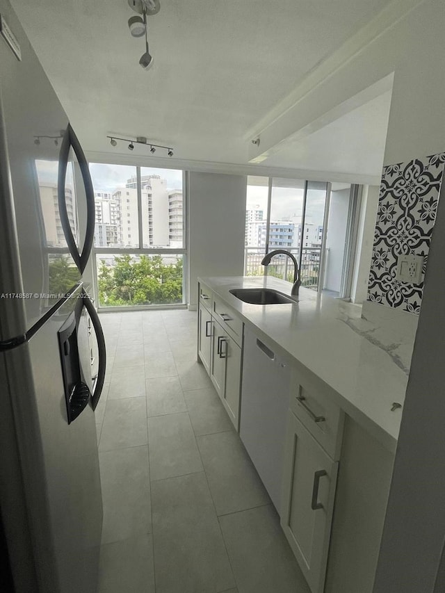 kitchen with sink, white dishwasher, stainless steel fridge, white cabinets, and light stone countertops