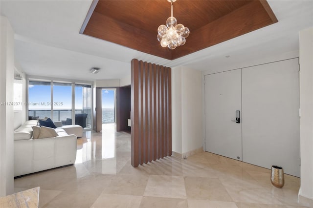 living room featuring wooden ceiling, a water view, a tray ceiling, a wall of windows, and a notable chandelier