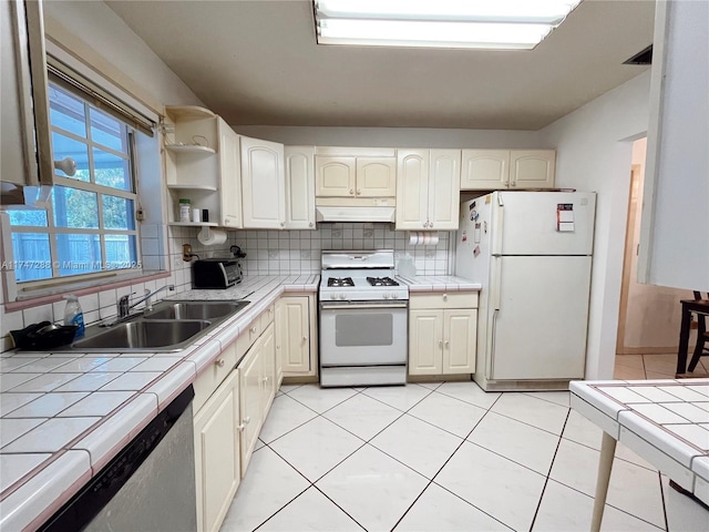 kitchen featuring white appliances, tile counters, backsplash, and sink