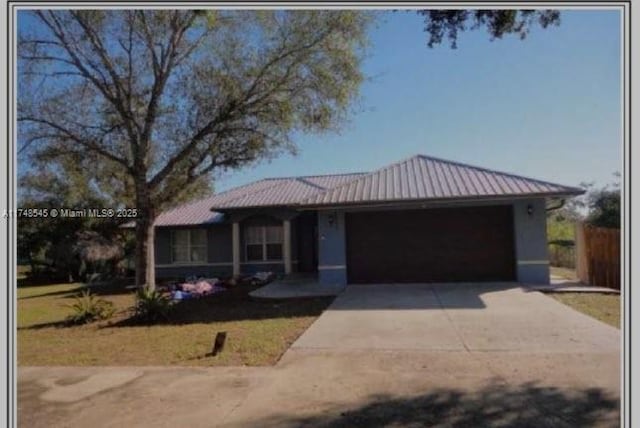 view of front of home with a garage, metal roof, driveway, and fence