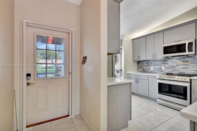 kitchen featuring stacked washing maching and dryer, stainless steel appliances, gray cabinetry, and lofted ceiling