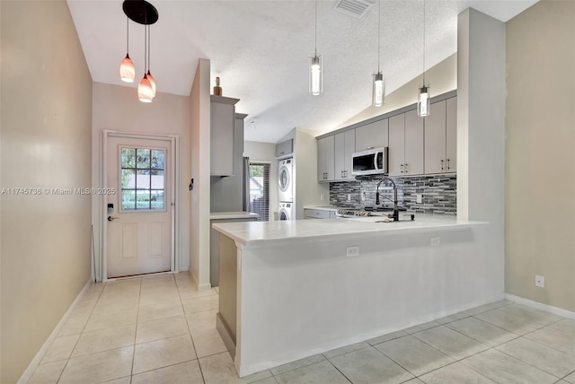 kitchen featuring vaulted ceiling, stacked washer and dryer, gray cabinetry, and kitchen peninsula