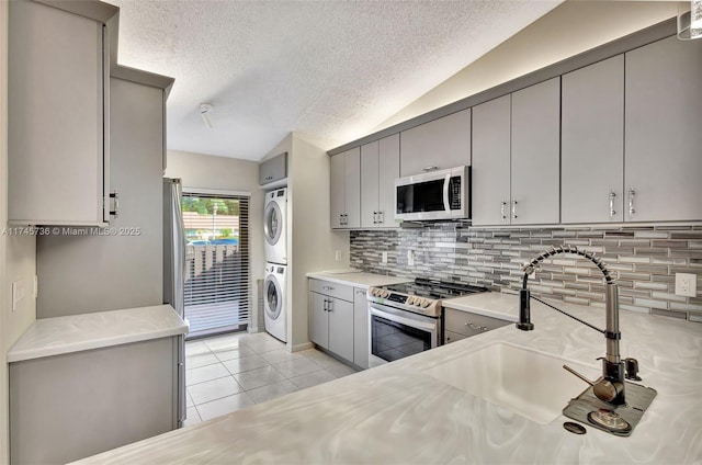 kitchen with stacked washer / dryer, electric stove, sink, lofted ceiling, and gray cabinets