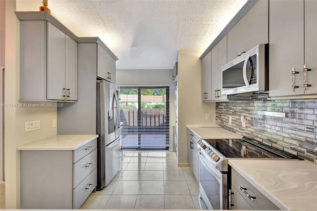 kitchen featuring backsplash, gray cabinetry, stainless steel appliances, and light tile patterned floors