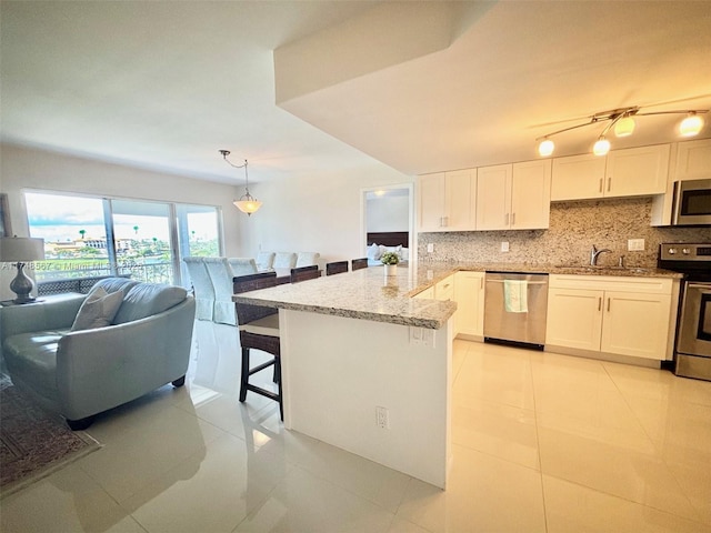 kitchen featuring a kitchen breakfast bar, stainless steel appliances, light stone countertops, decorative light fixtures, and white cabinetry