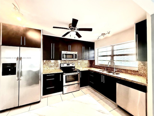 kitchen with appliances with stainless steel finishes, sink, light tile patterned floors, light stone countertops, and decorative backsplash