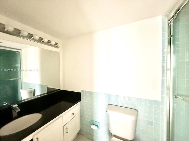 bathroom with toilet, vanity, tile walls, wainscoting, and a stall shower
