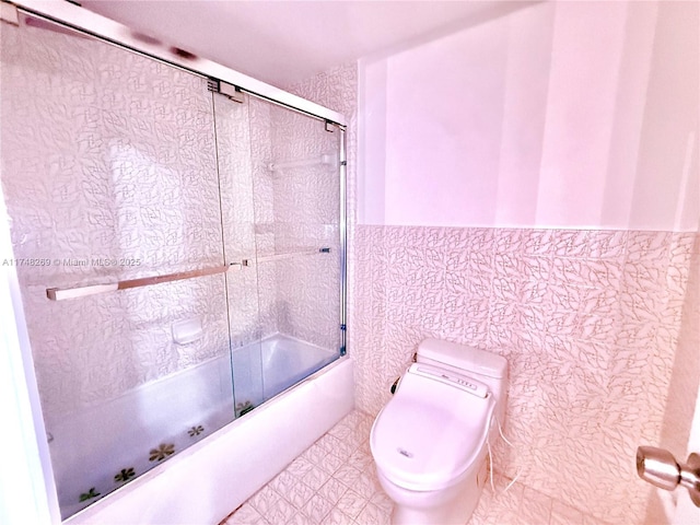 bathroom with tile walls, shower / bath combination with glass door, and toilet