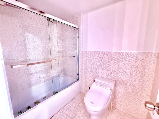 full bathroom with bath / shower combo with glass door, toilet, and tile walls