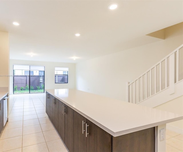 kitchen with white dishwasher, a kitchen island, light tile patterned flooring, and dark brown cabinets