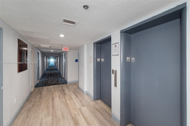 corridor featuring elevator, a textured ceiling, and light hardwood / wood-style flooring