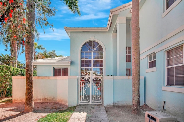 entrance to property with a gate, fence, and stucco siding