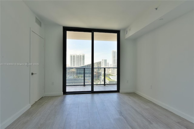 empty room with expansive windows, visible vents, light wood-type flooring, baseboards, and a city view