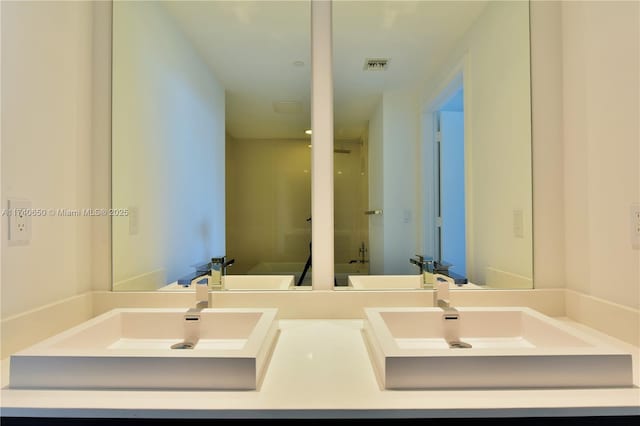 bathroom with double vanity, visible vents, walk in shower, and a sink