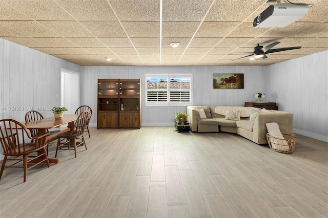 living area with baseboards, a drop ceiling, light wood-style floors, and a ceiling fan