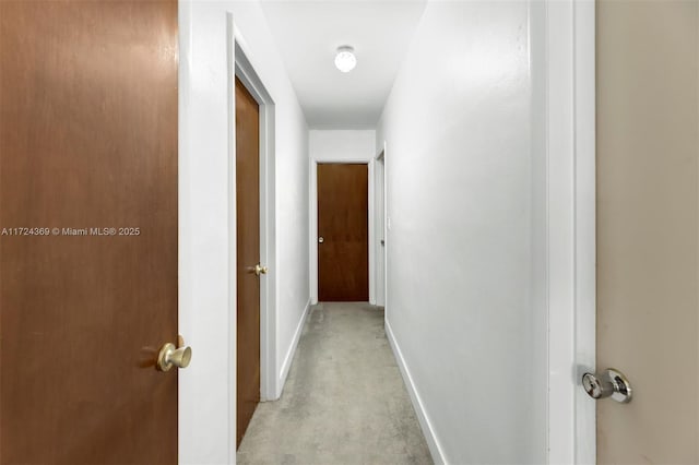 hallway with baseboards and light colored carpet
