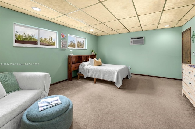 bedroom with a paneled ceiling, a wall mounted air conditioner, and light colored carpet