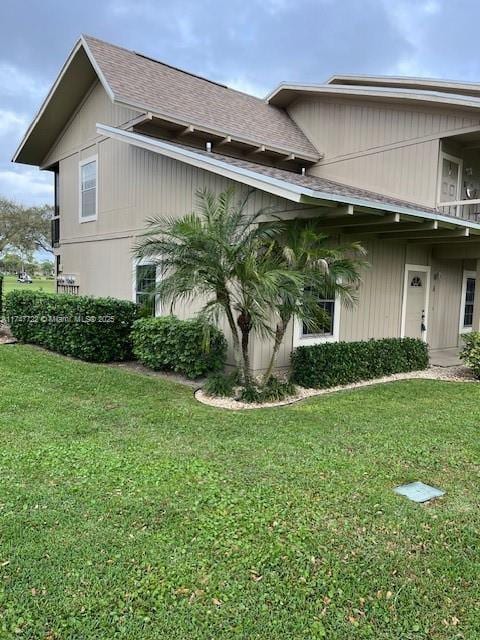 view of side of property with a shingled roof and a lawn