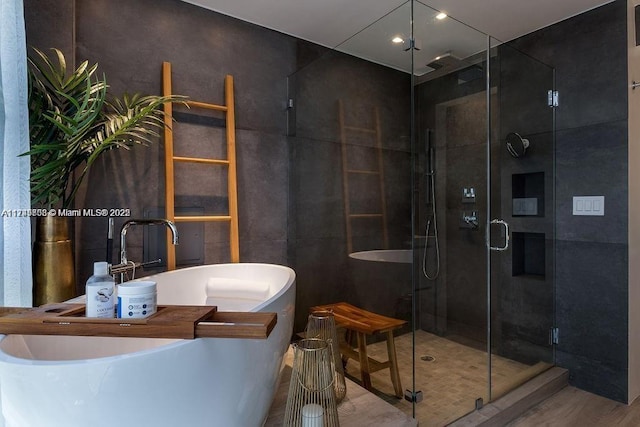 bathroom with a sink, a freestanding tub, a shower stall, and tile walls