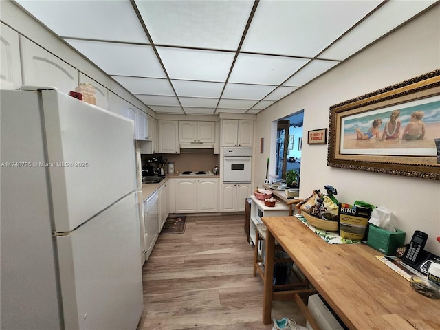 kitchen featuring white appliances, light wood finished floors, white cabinets, a drop ceiling, and butcher block countertops