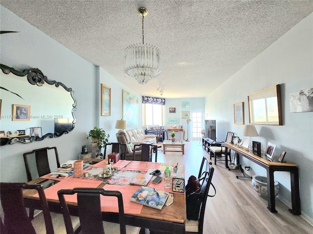 dining room with light wood finished floors, a textured ceiling, and an inviting chandelier