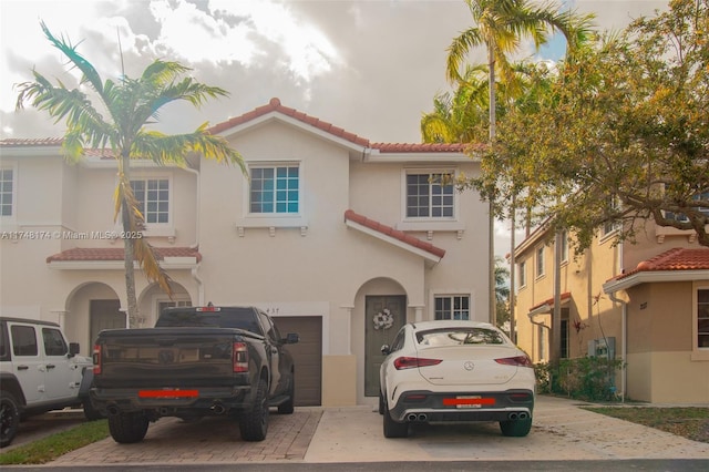 mediterranean / spanish-style home featuring a garage, decorative driveway, a tile roof, and stucco siding