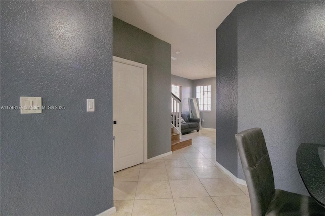 corridor with stairway, baseboards, and light tile patterned floors