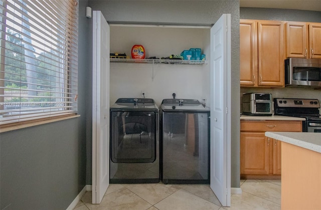 clothes washing area featuring laundry area, light tile patterned floors, baseboards, and washer and dryer