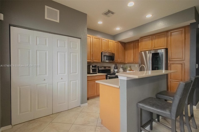 kitchen with visible vents, appliances with stainless steel finishes, a kitchen breakfast bar, a kitchen island with sink, and light countertops