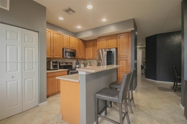 kitchen featuring light countertops, visible vents, appliances with stainless steel finishes, a kitchen island with sink, and a kitchen bar