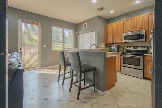 kitchen featuring light tile patterned floors, light countertops, visible vents, appliances with stainless steel finishes, and a kitchen breakfast bar