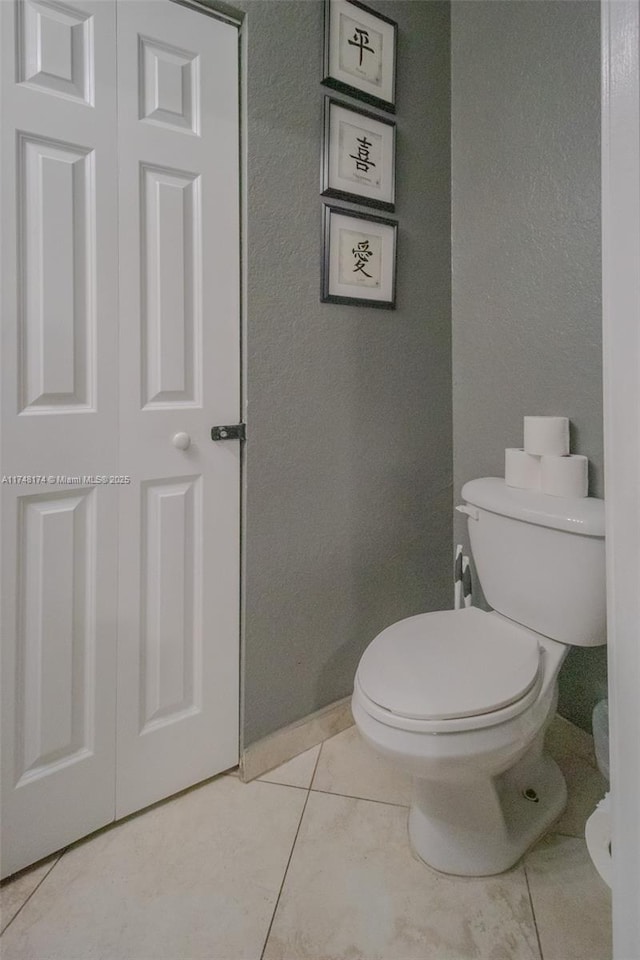 bathroom featuring a textured wall, tile patterned flooring, and toilet