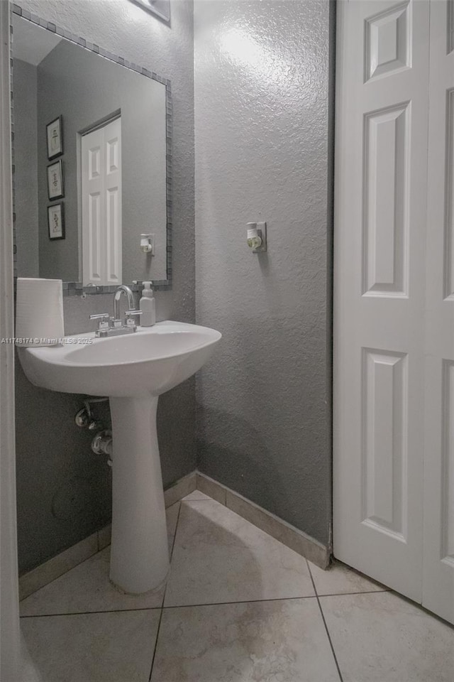 bathroom with baseboards, a textured wall, and tile patterned floors