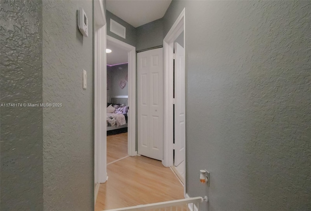 corridor featuring a textured wall, wood finished floors, and visible vents