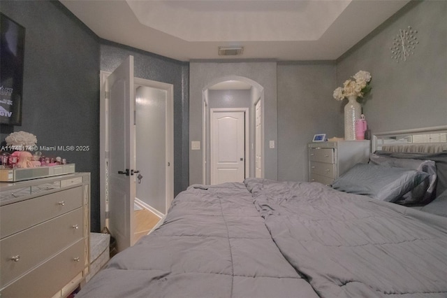 bedroom with visible vents, arched walkways, and a tray ceiling