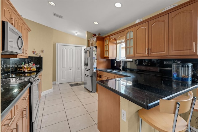 kitchen with glass insert cabinets, appliances with stainless steel finishes, a kitchen breakfast bar, a peninsula, and a sink