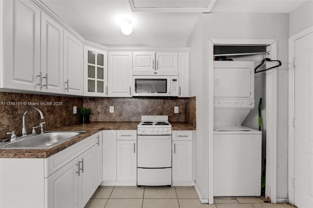 kitchen featuring glass insert cabinets, stacked washer / dryer, white cabinets, a sink, and white appliances