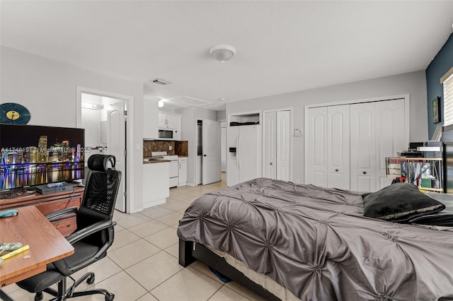 bedroom with white refrigerator with ice dispenser, light tile patterned floors, visible vents, and two closets