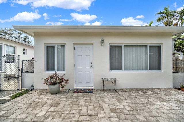 view of exterior entry with a patio area, fence, a gate, and stucco siding