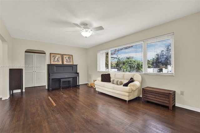 sitting room with a ceiling fan, arched walkways, dark wood-style flooring, and baseboards